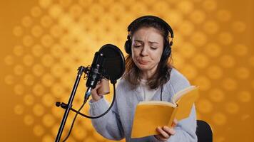 Voice actor reads book while enjoying coffee, recording audiobook using microphone, studio background. Woman using mic and headphones to produce digital recording of novel, drinking beverage, camera B photo