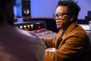 Audio technician and artist collaborating on music for pop rock album, processing and editing sounds with mixing console and software on computer. Singer works with producer for cool tracks. photo