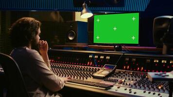 Sound designer watches online tutorials via greenscreen monitor to mix and master tracks and create music for his album. Audio engineer producing songs by twisting knobs and pushing faders. Camera B. photo