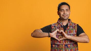 Portrait of jolly friendly indian man doing heart symbol shape gesture with hands. Cheerful nurturing person showing love gesturing, isolated over studio background, camera A photo