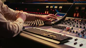 Audio technician uses mixing console and faders in control room, remote control for adjusting sound on mixer. Music producer changes volume level, creates tracks with technical equipment. Camera B. photo