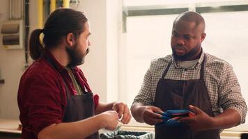 Master in woodworking shop giving BIPOC worker protection gloves before assembling furniture. Cabinetmaker preparing safety equipment for african american apprentice before starting work, camera A photo