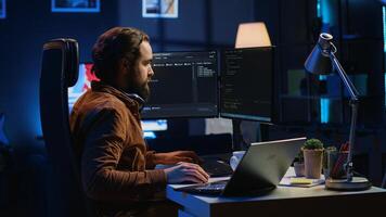 Technician typing code in neon lit personal office, using javascript programming language to develop software application. It specialist using multimonitor desktop setup to finish project, camera A photo