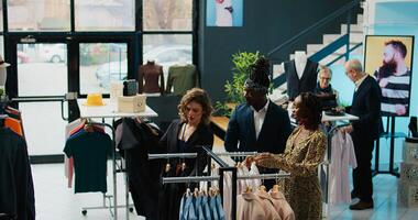 Employees team assisting pregnant woman to find trendy clothes, showing multiple models and colors on hangers. Retail assistants making suggestions for african american customer at store. Camera B. photo