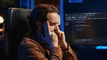 Annoyed software technician rubbing temples in frustration after failing to remove bugs appearing while coding on computer. Teleworker feeling irked by script errors, closing eyes, camera A photo