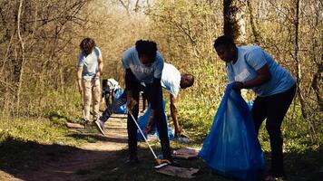 Environmental activists collecting rubbish and plastic waste in garbage bag, using littler cleanup tools to pick up trash from the forest. Women doing voluntary work to protect ecosystem. Camera B. photo