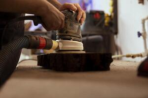 Carpenter using orbital sander with fine sandpaper on lumber piece to achieve refined finish. Manufacturer using angle grinder on wood block for professional results, close up shot photo