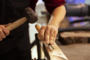 Man carving intricate designs into wood using chisel and hammer in carpentry shop, enjoying diy hobby. Woodworking specialist in studio shaping wooden pieces with tools, making wood art, close up shot photo