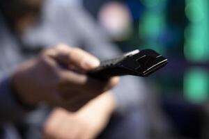 Focus on pointer device used by man in blurry background to zap through channels, resting in living room. Close up shot on remote control used by viewer to select TV station on television set photo