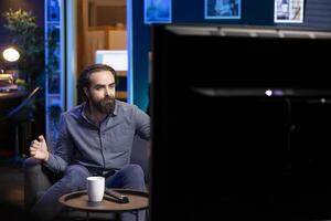 Man watching TV shows at home in living room, paying close attention to screen. Man relaxing in apartment on couch, enjoying fascinating film plot and characters on television series photo