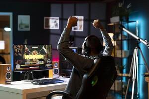 Gamer celebrating winning multiplayer science fiction videogame tournament, playing with friends online. Man happy about gaming championship victory, using headphones to chat with teammates photo