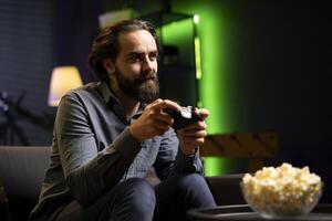 Man holding controller in green neon illuminated apartment, playing videogames. Gamer on couch using joystick to participate in PvP online multiplayer game on console system, relaxing and having fun photo