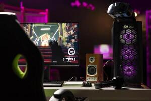 Empty neon lit living room with RGB lit computer on table next to headphones and high tech VR headset. FPS videogame left open on desktop pc display and virtual reality glasses in apartment photo