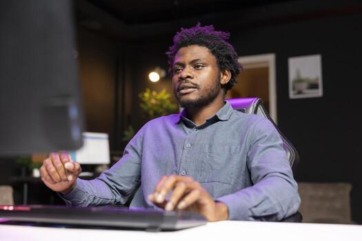 Gamer playing videogames on computer desktop late at night, struggling to stay awake. Man using PC keyboard and mouse to try and finish game mission before going to sleep photo
