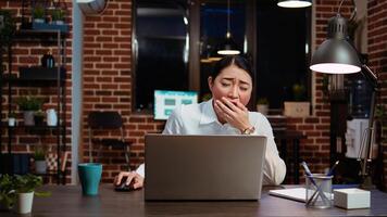 Employee tired while writing emails at computer desk, trying to freshen up by drinking coffee. Exhausted worker working overnight, typing on laptop, trying to get energy from caffeine, camera A photo