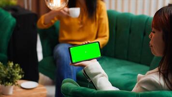 Asian woman holding phone with isolated greenscreen in lobby, looking at display with chromakey template and mockup copyspace layout. Traveler using device and relaxing at hotel. photo
