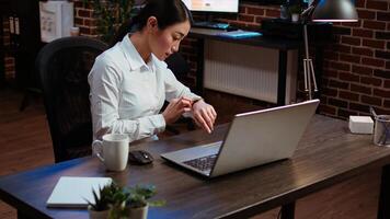 Sleepy employee asleep on computer desk at night in brick wall office, suddenly waking up. Tired businesswoman looking at watch, annoyed by time passing too slow while working overnight, camera A photo