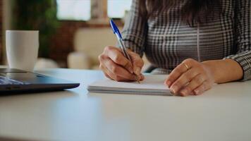 Teleworker at desk transcribing data from laptop to notepad, finalizing project. Remote worker solving job tasks before deadline, writing info on paper using pen, camera A close up panning shot photo
