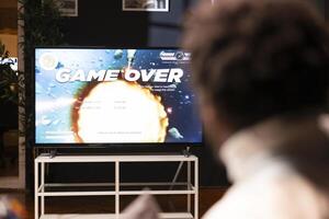 BIPOC gamer feeling gutted after losing singleplayer science fiction videogame level, being outsmarted by enemies. Man at home frustrated after seeing game over screen on smart TV display photo