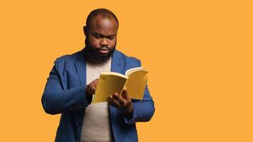 Man struggling to read book with small font, pointing finger to words on page. Person enjoying literature novel, wetting fingers to change page, isolated over studio background, camera A photo