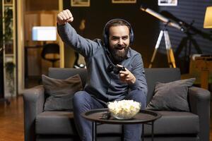Gamer feeling relieved after winning videogame level, screaming at television set in excitement. Pleased man at home yelling from joy after seeing achieving victory while playing on gaming console photo