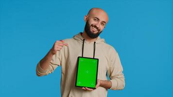 Muslim person holding tablet with greenscreen template, presenting isolated copyspace on device display. Middle eastern guy using gadget to create commercial ad with chromakey. Camera 1. photo