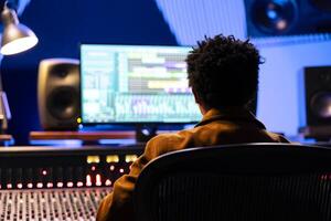 African american record composer mixing and mastering songs with audio software, working with auto sliders and buttons to adjust sound volume levels. Sound engineer creating new music. photo