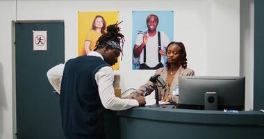 Retail employee picking up clothes order boxes from department store, signing invoice and confirmation papers at cash register counter. African american woman giving requested merchandise. Camera B. photo