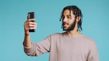 Happy man chatting with friend over online videocall on smartphone, doing friendly gestures. Smiling person communicating with mate using mobile phone teleconference, studio background, camera B photo