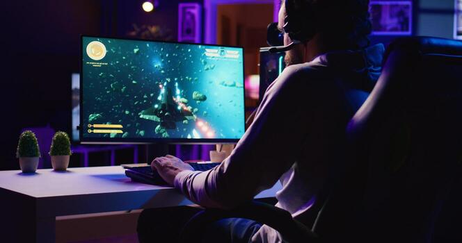 Man in dimly lit apartment playing singleplayer videogame with spaceship shooting laser streams at asteroid. Gamer using crosshair overlay to hit targets in science fiction arcade game photo