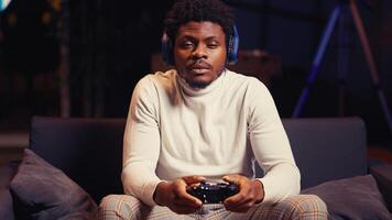 Portrait of BIPOC man wearing headphones and playing intense online videogame, spamming buttons on controller. Gamer participating in internet esports competition, playing on gaming console, close up photo