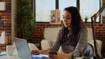 Happy woman stoked on doing online shopping, carefully typing credit card information on laptop. Indian person adding payment method on website while in cozy stylish warm home, camera B panning shot photo