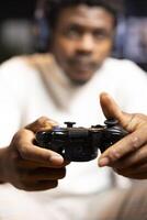 Focus shot on controller held by man defeating enemies while playing videogames on gaming console with teammates. Player in blurry background using gamepad to participate in esports game photo