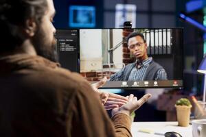 Cybersecurity professional helped by coworker during internet videocall to look for company security loopholes and injected viruses. Engineer and colleague in remote videoconference writing code on PC photo