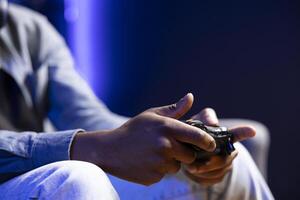 Gamer in RGB lit home gaming with gamepad, enjoying himself. Close up shot of man sitting on sofa in neon illuminated living room, playing videogames on console using controller photo
