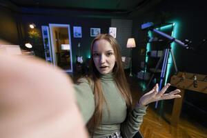 POV of social media star using cellphone camera to capture welcoming intro for vlogging channel. Girl in home studio connecting with loyal audience during livestream, filming with selfie stick photo