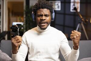 Cheerful gamer bragging after finally defeating all enemies while playing on gaming console. Joyful african american man congratulating himself after winning videogame using controller photo
