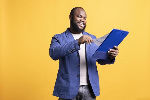 Smiling man satisfied with work done on financial audit report pages, happy with good job, studio background. Joyful manager pleased with high company profits while reading paperwork photo