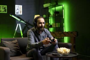 Smiling man focused on defeating enemies while playing videogames on gaming console with teammates, talking through headphones. Happy gamer fights rival players and chats with friends through headset photo