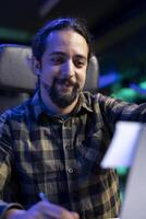 Closeup of smiling male freelancer putting sticky note on his laptop screen while working from home. Young man looking at his notes on paper for studying and researching. photo