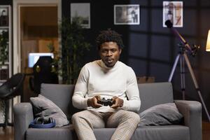Player using controller to play videogame on gaming console in cozy apartment. African american gamer using high tech gamepad to destroy enemies, relaxing at home on couch photo