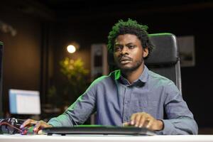 BIPOC man in living room playing games on gaming PC at computer desk all day, feeling tired. Gamer strained and exhausted after contending against foes in online multiplayer shooter photo