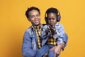 African american dad and his child playing with a flashlight on camera, sweet boy wearing headset while his father is carrying him around the studio. Adorable kid discovering a lamplight. photo