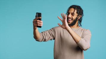 Happy man chatting with friend over online videocall on smartphone, doing friendly gestures. Smiling person communicating with mate using mobile phone teleconference, studio background, camera A photo