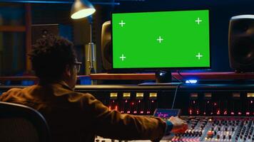 Audio technician works on music post production with greenscreen in control room, pushing sliders and faders to adjust volume level. Producer mixing and mastering tracks with console in studio. Camera B. photo