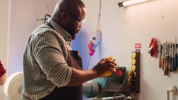 BIPOC man in studio with woodworking tools in background using sandpaper for sanding wooden surface. Woodworking expert using abrasive sponge to fix damages suffered by piece of wood, camera A photo