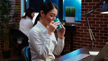 Employee enjoying cup of coffee while analyzing sales reports to plan business development. Office employee drinking hot beverage while using laptop to do project research photo
