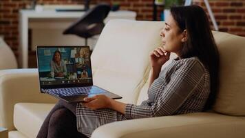 Indian remote professional holding q and a session with multiethnic webinar participants via teleconference meeting. Internet videocall host on couch at home engaging in discussions with trainees photo