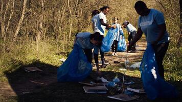 Group of diverse volunteers collecting rubbish from the woods and recycling in a garbage disposal bag, litter cleanup responsibility. Ecology activists picking up trash and plastic waste. Camera B. photo