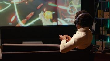 Man playing singleplayer videogames on ultrawide smart TV, putting headphones on to feel immersed. BIPOC gamer using controller to beat science fiction shooter game on gaming console photo